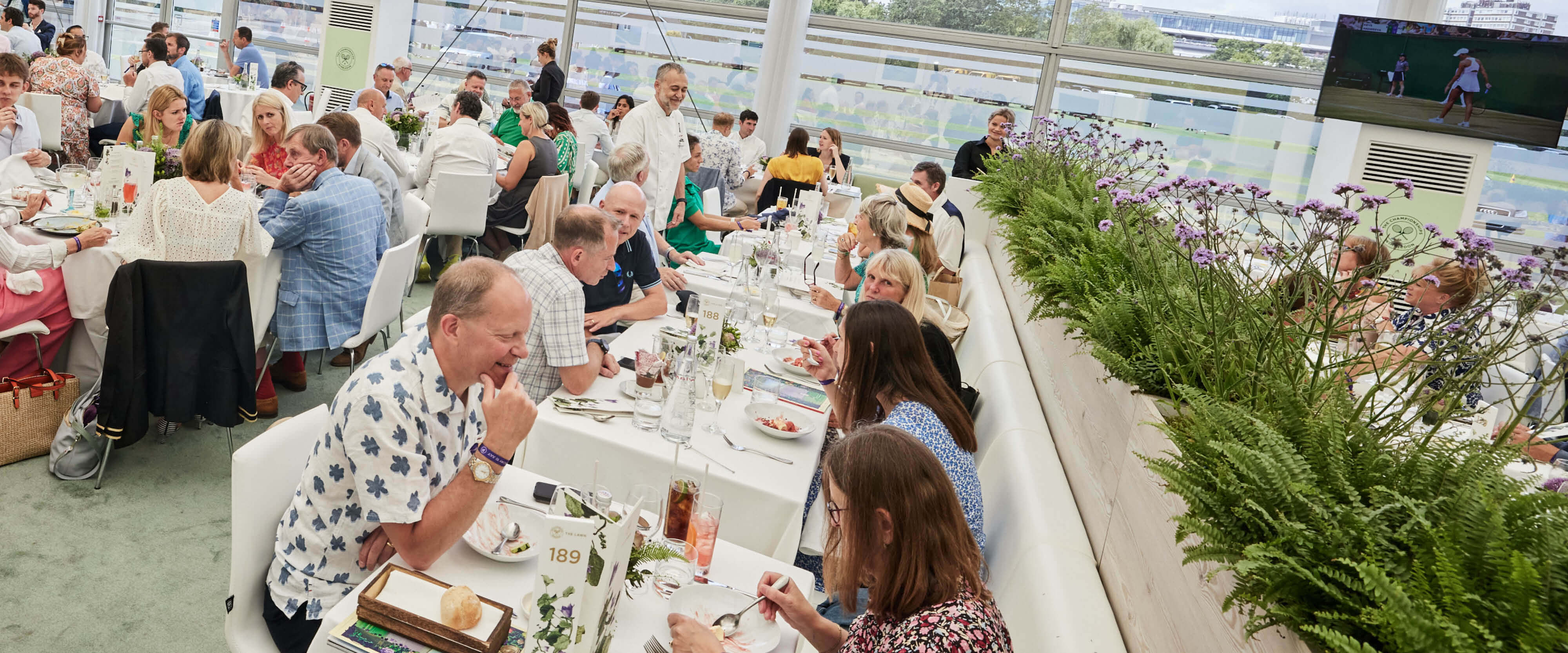 Guests seated eating lunch inside The Lawn hospitality facility with Michelin Star Chef Michel Roux Jr going round talking to guests at their tables at The Championships Wimbledon